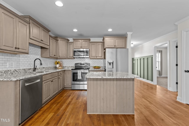 kitchen with sink, light stone counters, a kitchen island, crown molding, and appliances with stainless steel finishes