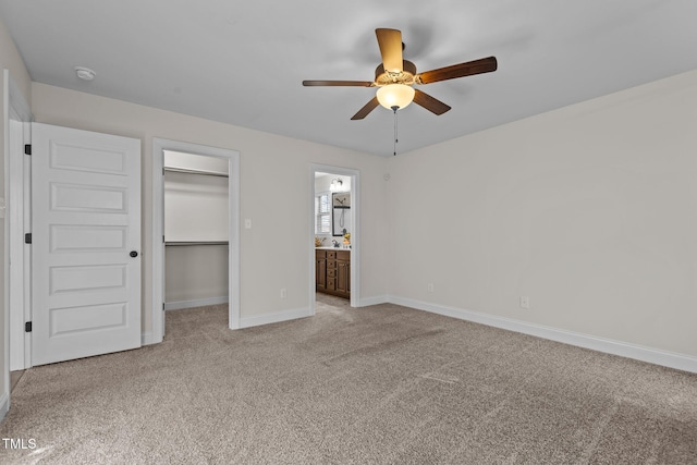 unfurnished bedroom featuring ensuite bath, a closet, a walk in closet, ceiling fan, and light carpet