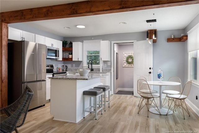 kitchen with decorative light fixtures, stainless steel appliances, a kitchen island, white cabinetry, and dark stone counters