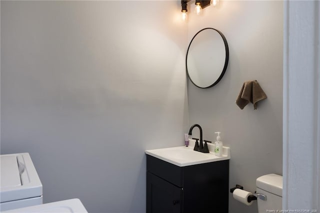 bathroom with toilet, vanity, and washer / dryer