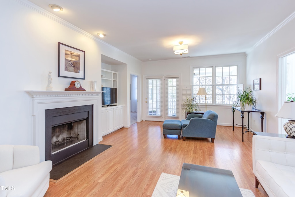 living room with light hardwood / wood-style flooring, crown molding, and built in shelves