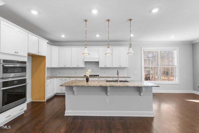 kitchen featuring white cabinetry, light stone countertops, an island with sink, and a sink