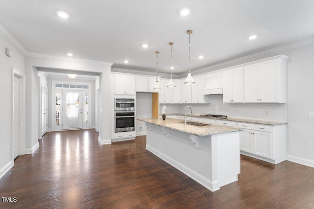 kitchen featuring white cabinetry, hanging light fixtures, a center island with sink, and a sink