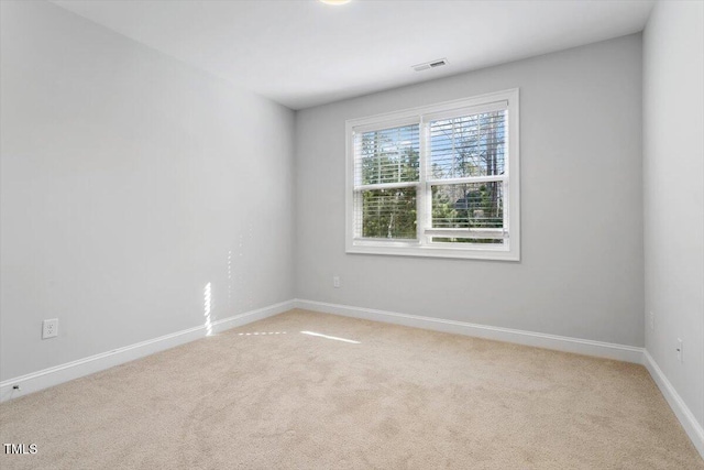 spare room featuring light colored carpet, visible vents, and baseboards