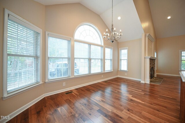 unfurnished dining area featuring high vaulted ceiling, dark wood-type flooring, a notable chandelier, and a fireplace