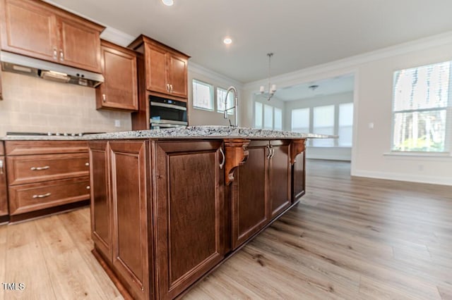 kitchen with oven, an island with sink, black electric cooktop, hanging light fixtures, and a notable chandelier