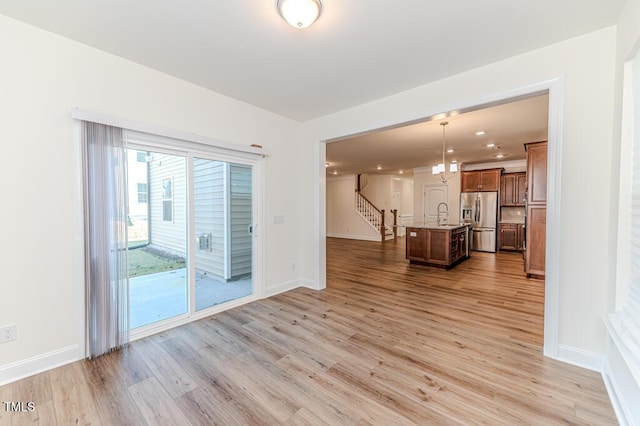 unfurnished living room featuring sink, light hardwood / wood-style floors, and a notable chandelier