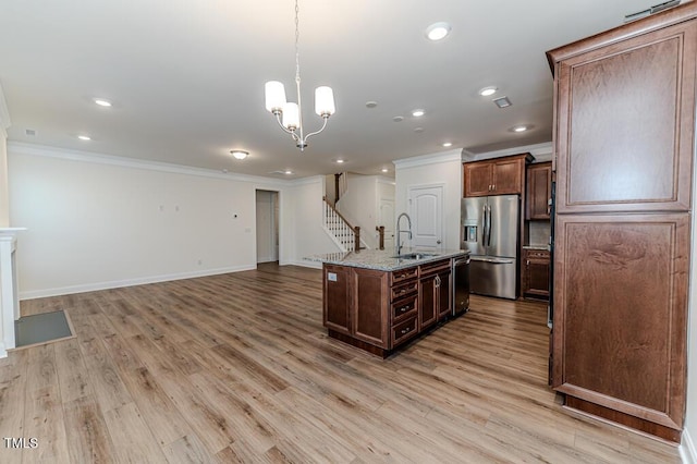 kitchen featuring light stone counters, pendant lighting, a center island with sink, appliances with stainless steel finishes, and sink