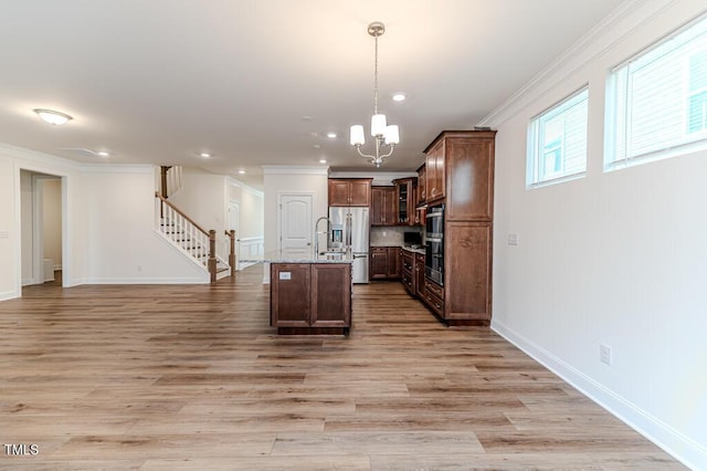 kitchen featuring stainless steel appliances, ornamental molding, light hardwood / wood-style floors, hanging light fixtures, and a center island with sink