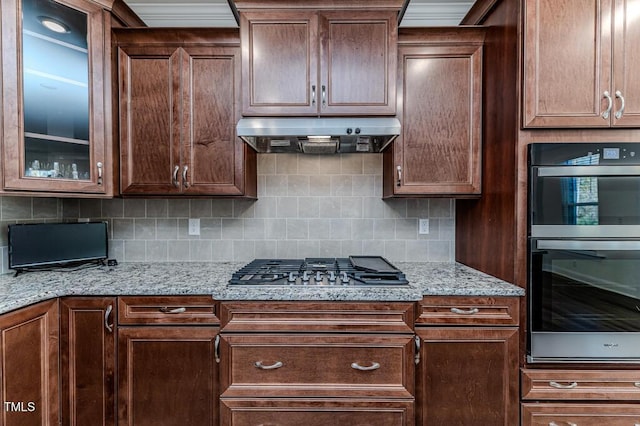 kitchen featuring light stone counters, stainless steel appliances, range hood, and backsplash