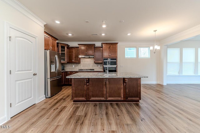 kitchen with stainless steel appliances, a kitchen island with sink, crown molding, and light stone countertops