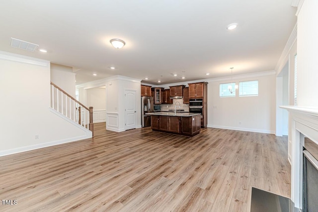 kitchen with light hardwood / wood-style flooring, hanging light fixtures, a high end fireplace, a kitchen island with sink, and appliances with stainless steel finishes