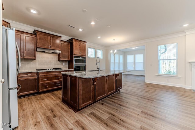 kitchen with a kitchen island with sink, stainless steel appliances, light stone countertops, pendant lighting, and sink