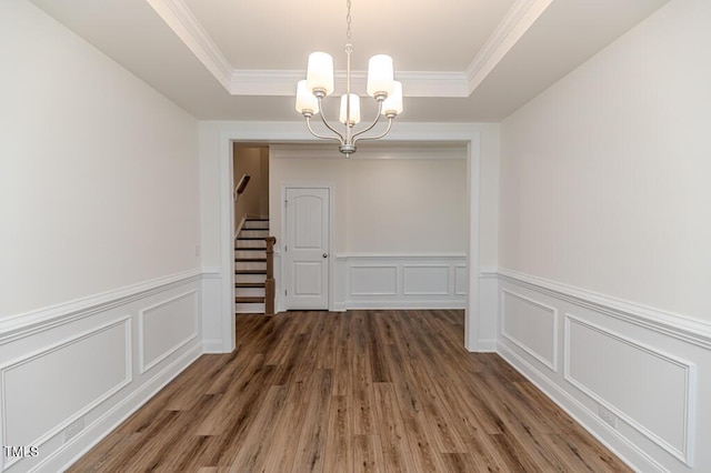 unfurnished dining area featuring a raised ceiling, crown molding, a notable chandelier, and dark hardwood / wood-style floors