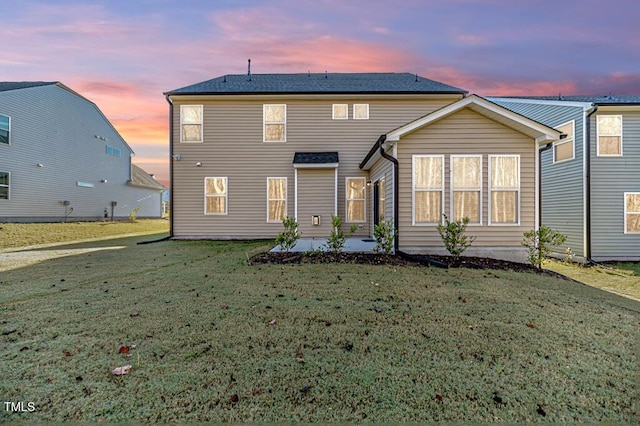 back house at dusk with a lawn and a patio area