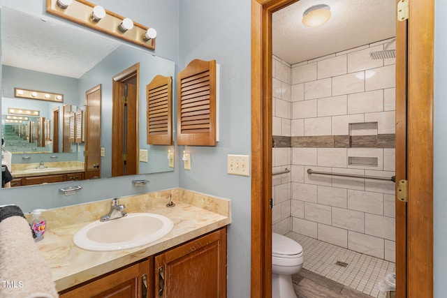 bathroom featuring a textured ceiling, toilet, vanity, and a tile shower