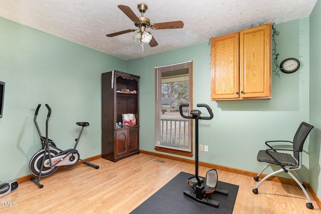 exercise area with ceiling fan, light wood-type flooring, and a textured ceiling