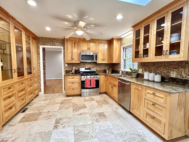 kitchen featuring backsplash, appliances with stainless steel finishes, a sink, ceiling fan, and dark stone counters