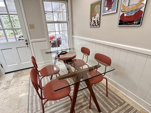 dining area featuring a wealth of natural light, stone finish floor, and wainscoting