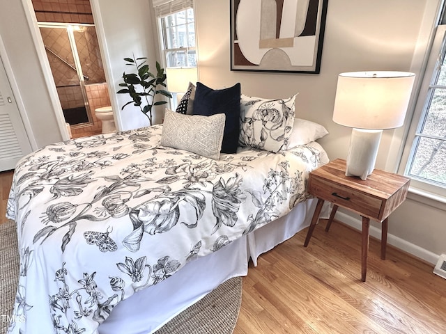 bedroom with ensuite bath, wood finished floors, visible vents, and baseboards