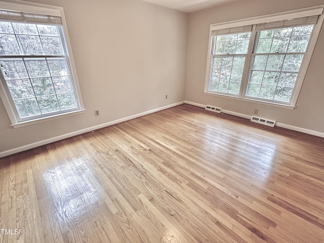 unfurnished room featuring hardwood / wood-style floors, plenty of natural light, visible vents, and baseboards