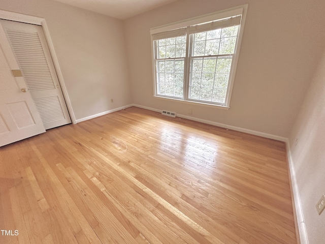 unfurnished bedroom featuring baseboards, a closet, visible vents, and light wood-style floors