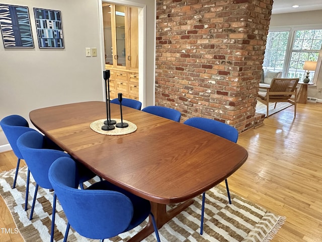 dining area featuring light wood-style floors, baseboards, and brick wall