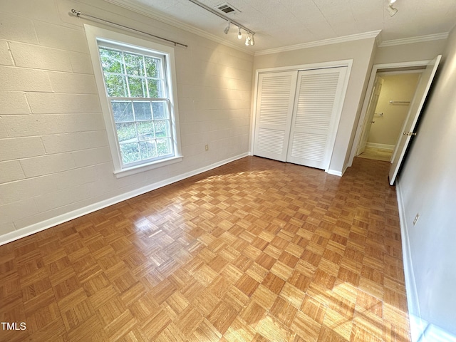 unfurnished bedroom with concrete block wall, baseboards, a closet, rail lighting, and crown molding