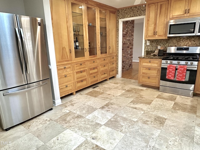 kitchen with stainless steel appliances, dark countertops, decorative backsplash, glass insert cabinets, and stone finish flooring