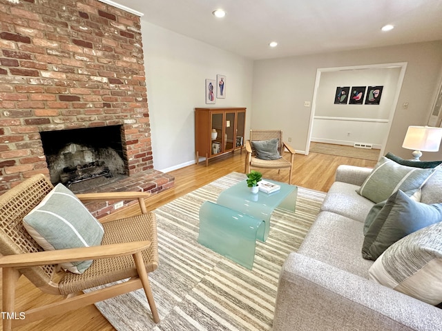 living area featuring baseboards, visible vents, wood finished floors, a brick fireplace, and recessed lighting