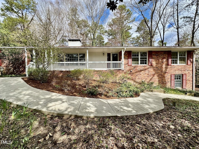 view of front of property featuring covered porch, a chimney, and brick siding