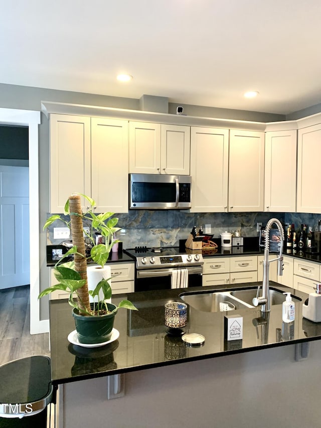 kitchen with hardwood / wood-style floors, white cabinets, stainless steel appliances, dark stone counters, and decorative backsplash