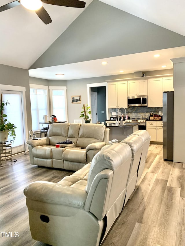 living room featuring ceiling fan, light wood-type flooring, and high vaulted ceiling