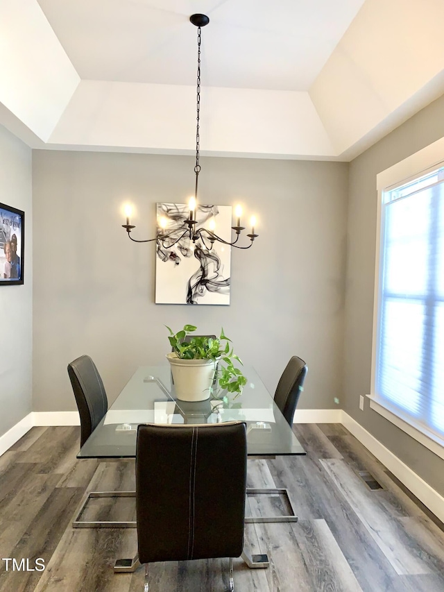 dining room with dark hardwood / wood-style floors, a raised ceiling, and a chandelier