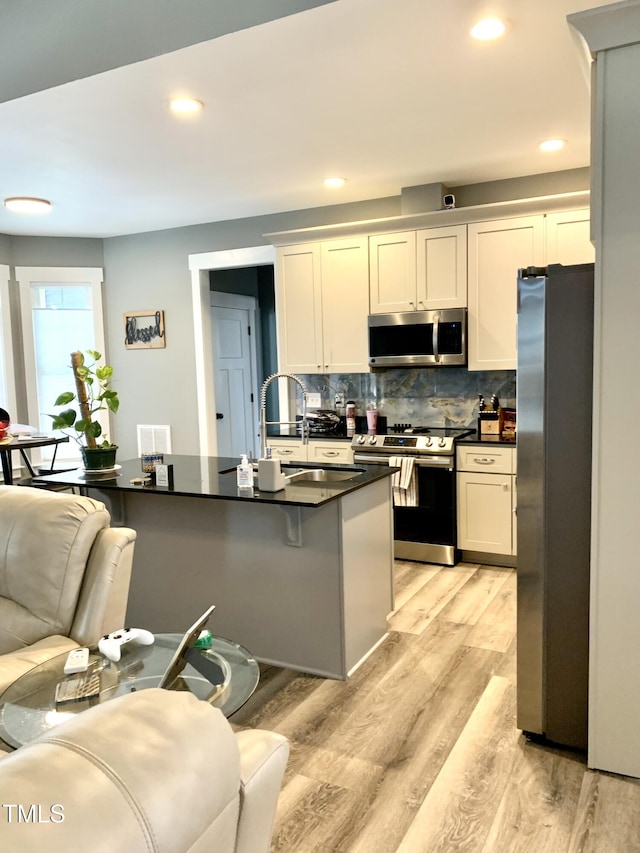 kitchen featuring decorative backsplash, white cabinetry, light hardwood / wood-style flooring, appliances with stainless steel finishes, and a kitchen breakfast bar