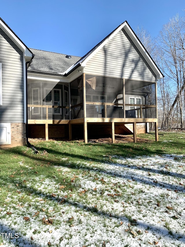 snow covered rear of property featuring a yard and a sunroom