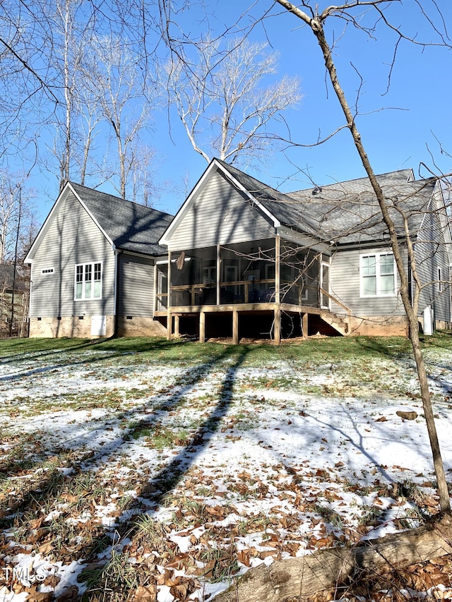 snow covered rear of property featuring a sunroom