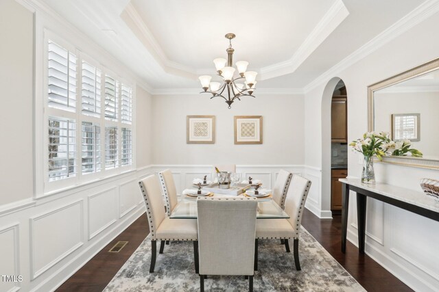 dining room featuring a notable chandelier, a tray ceiling, dark wood-style floors, arched walkways, and a decorative wall