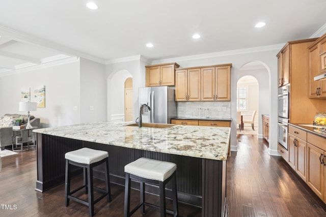 kitchen with a sink, a kitchen breakfast bar, arched walkways, and appliances with stainless steel finishes