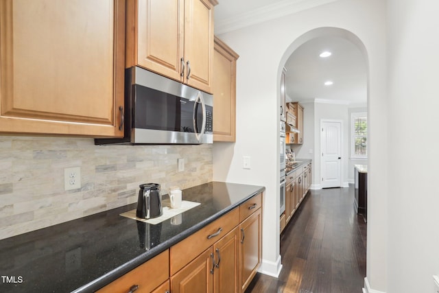 kitchen with dark wood finished floors, stainless steel appliances, dark stone counters, crown molding, and decorative backsplash