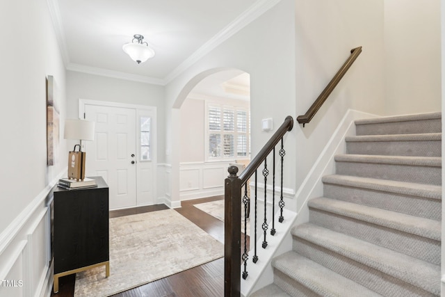 entryway featuring stairway, dark wood finished floors, arched walkways, ornamental molding, and a decorative wall