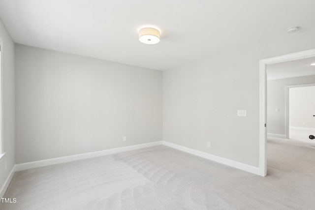 spare room featuring light colored carpet and baseboards