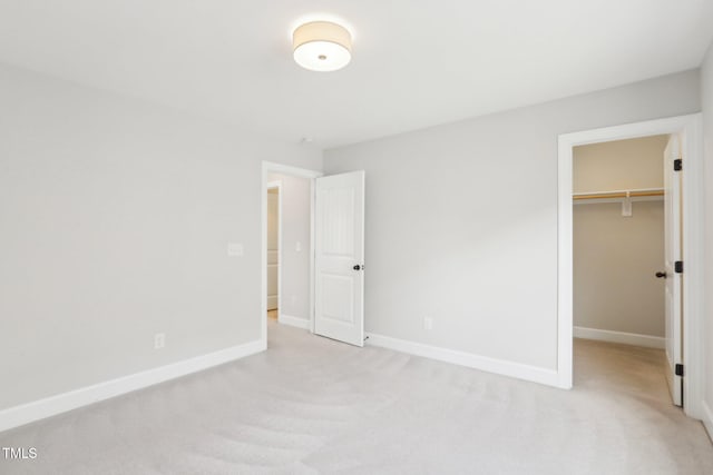 unfurnished bedroom featuring a closet, light colored carpet, a walk in closet, and baseboards