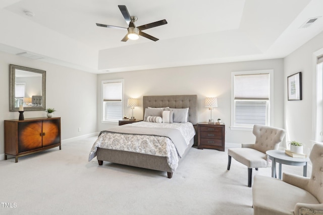 bedroom with a ceiling fan, visible vents, baseboards, a tray ceiling, and light carpet