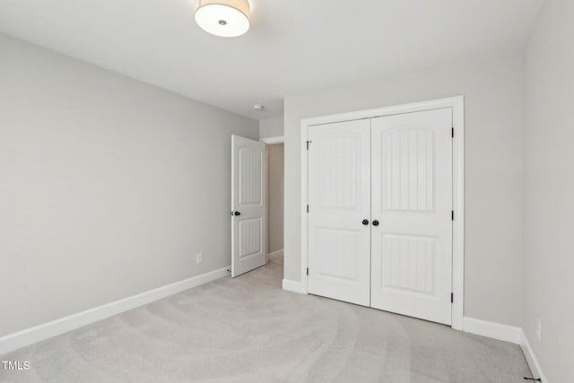 unfurnished bedroom with light carpet, a closet, and baseboards