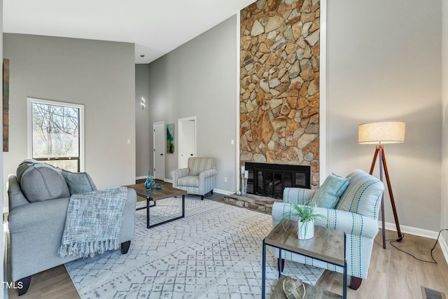 living room featuring high vaulted ceiling, a fireplace, and light hardwood / wood-style flooring