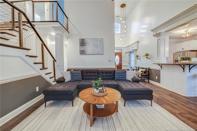 living room featuring a towering ceiling, hardwood / wood-style floors, ornamental molding, and decorative columns