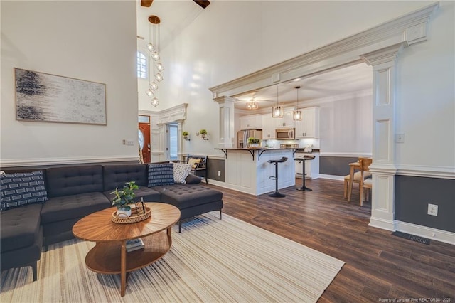 living room with a towering ceiling, dark wood-type flooring, ornamental molding, and decorative columns