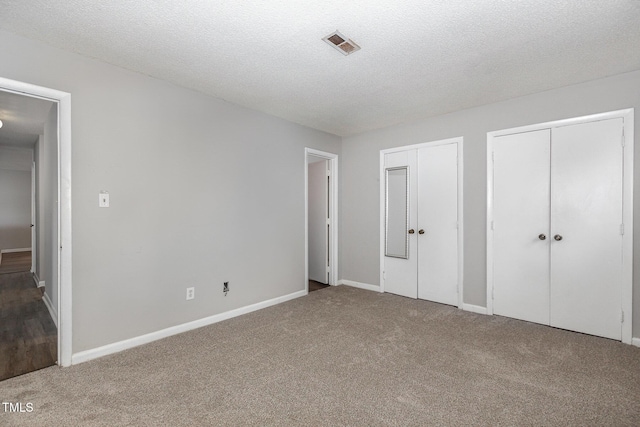 unfurnished bedroom featuring carpet flooring, two closets, and a textured ceiling