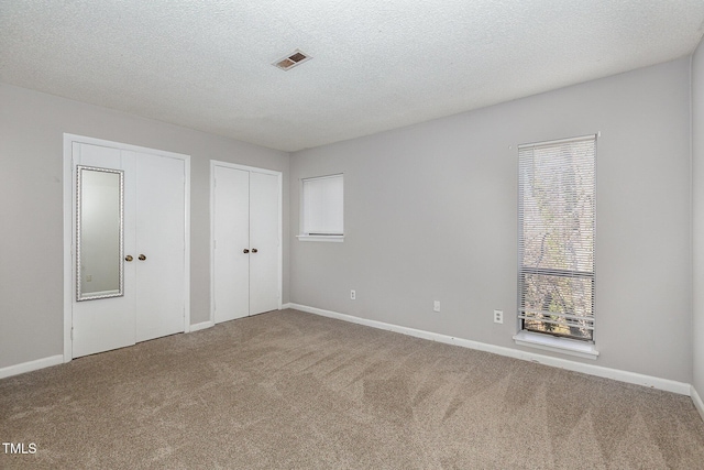 unfurnished bedroom with carpet flooring, two closets, and multiple windows